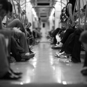 imagem 2 imagem em preto e branco de um vagão de trem. Nos dois cantos da imagem, há pessoas sentadas de perfil, com mãos e pernas em dife