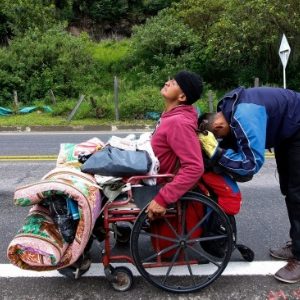 15set2018-migrante-venezuelano-jefferson-alexis-e-seu-pai-jose-agustin-lopez-na-cadeira-de-rodas-param-para-descansar-na-estrada-rumo-a-pamplonana-colombia-1537376385423_615x300